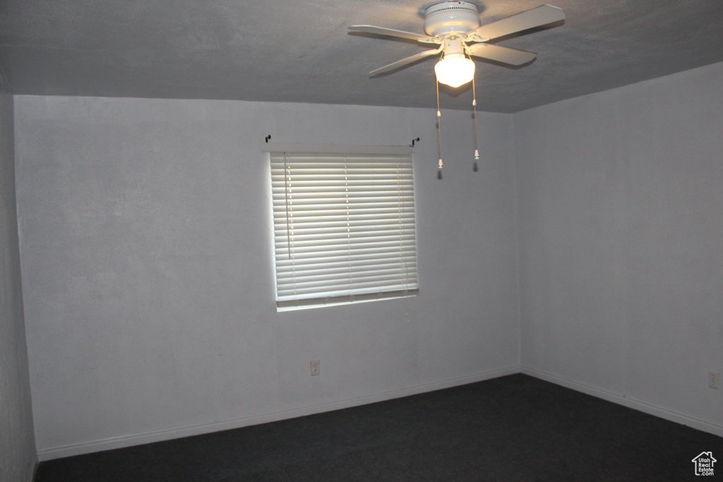 Empty room with ceiling fan and dark colored carpet