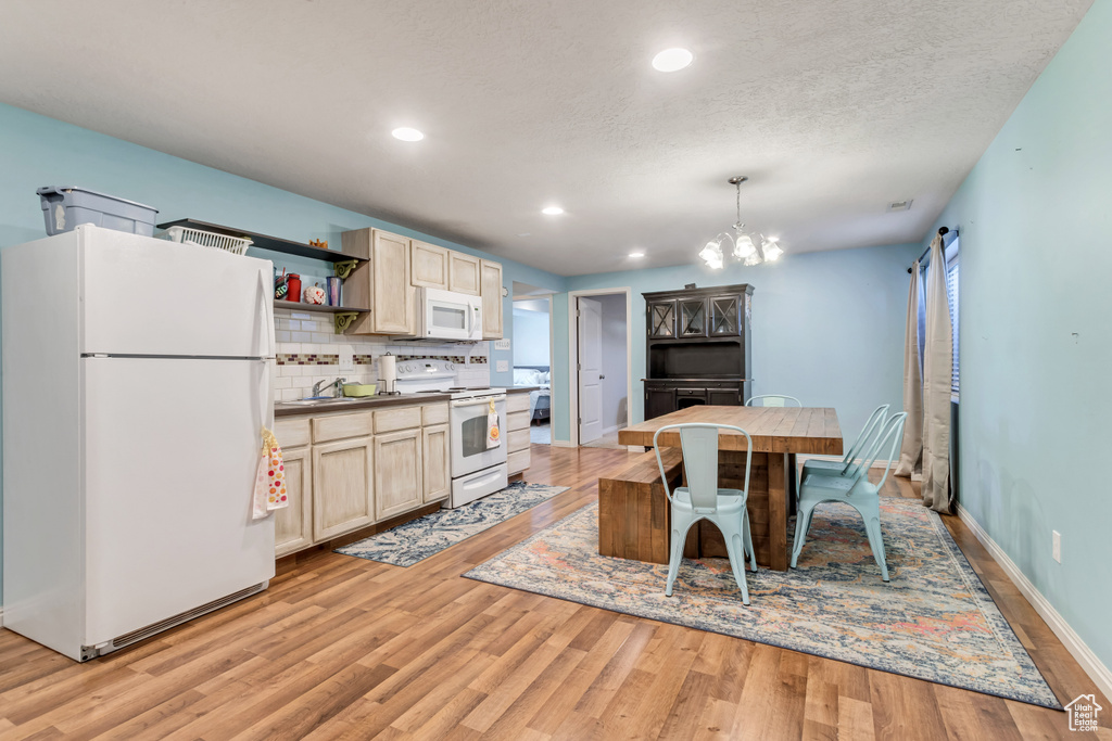 Kitchen with light brown cabinets, white appliances, light hardwood / wood-style flooring, tasteful backsplash, and a chandelier