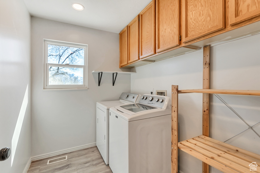 Laundry room with light hardwood / wood-style flooring, washing machine and clothes dryer, and cabinets