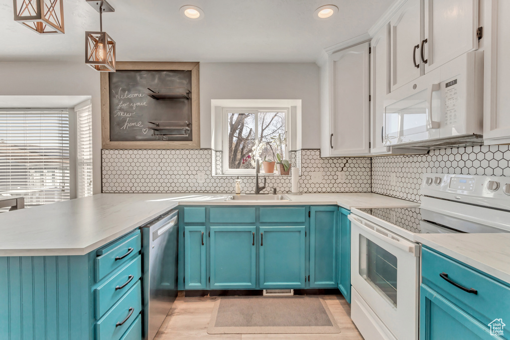 Kitchen with tasteful backsplash, white appliances, blue cabinetry, and pendant lighting