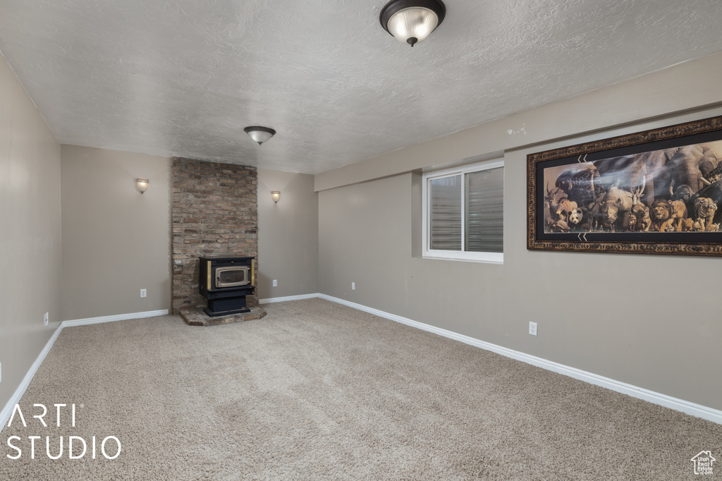 Unfurnished living room with a textured ceiling, light colored carpet, and a wood stove
