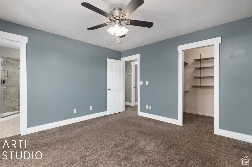 Unfurnished bedroom with dark colored carpet, ensuite bathroom, ceiling fan, a closet, and a walk in closet