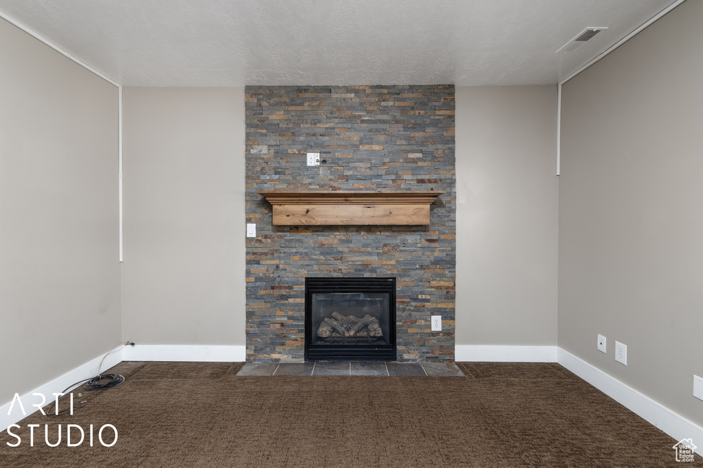 Unfurnished living room with a textured ceiling, dark carpet, and a fireplace