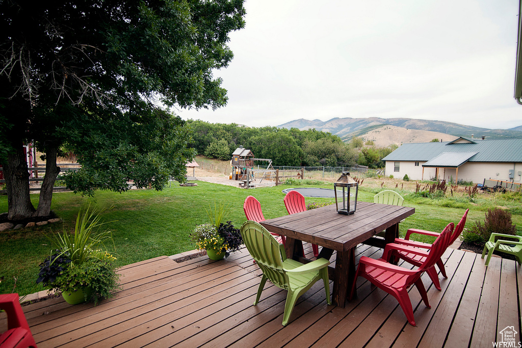 Deck with a playground, a mountain view, and a yard
