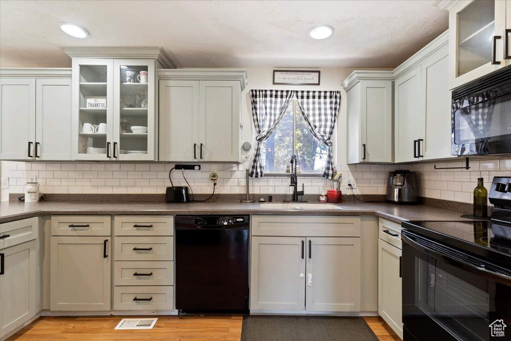 Kitchen with light hardwood / wood-style floors, tasteful backsplash, black appliances, and sink