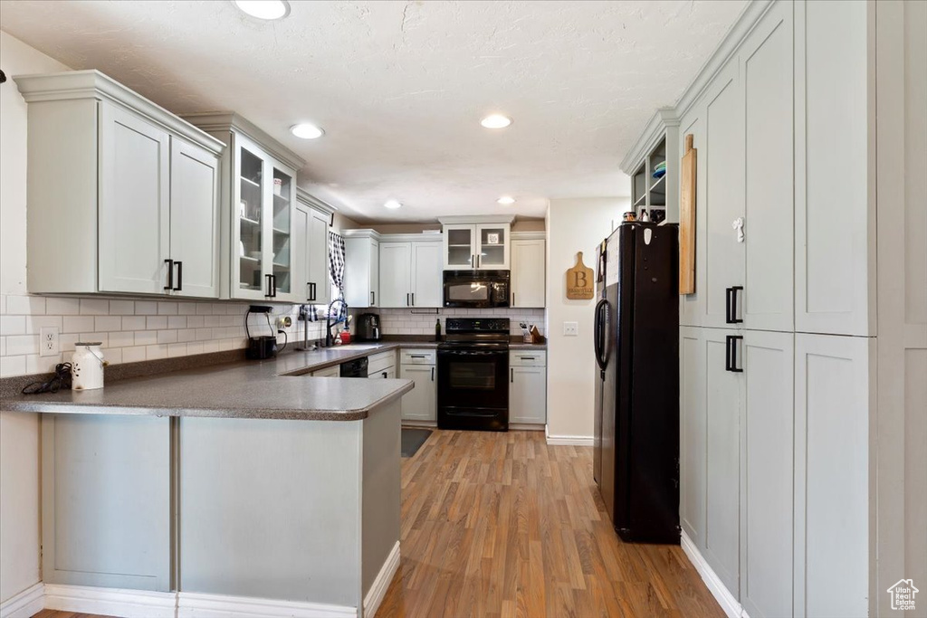 Kitchen featuring kitchen peninsula, tasteful backsplash, light hardwood / wood-style flooring, black appliances, and white cabinetry