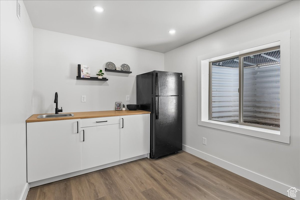 Kitchen featuring black refrigerator, sink, white cabinetry, and light hardwood / wood-style flooring