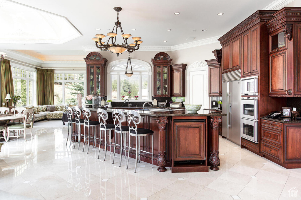 Kitchen featuring pendant lighting, an island with sink, a notable chandelier, light tile floors, and stainless steel built in refrigerator
