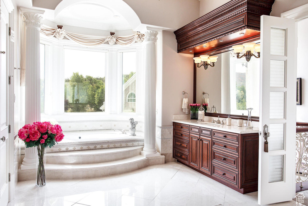 Bathroom featuring tiled tub, tile flooring, decorative columns, and oversized vanity