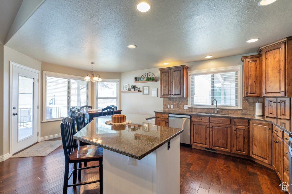 Kitchen featuring a center island, tasteful backsplash, dark wood-type flooring, dishwasher, and an inviting chandelier