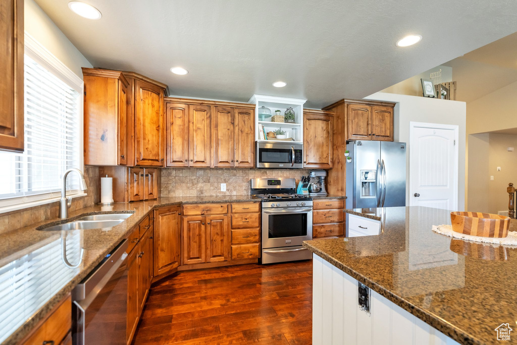 Kitchen featuring dark stone counters, tasteful backsplash, appliances with stainless steel finishes, dark hardwood / wood-style flooring, and sink