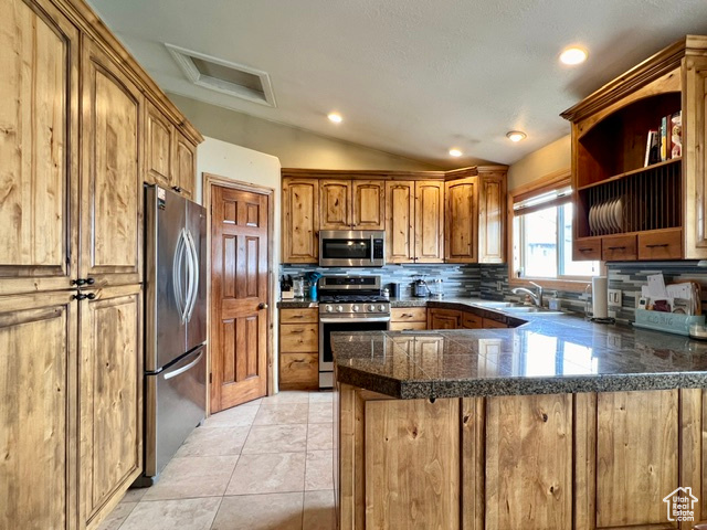 Kitchen with kitchen peninsula, backsplash, stainless steel appliances, light tile flooring, and vaulted ceiling