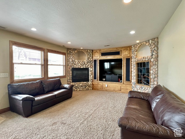 Living room with light colored carpet, a textured ceiling, built in shelves, and a fireplace