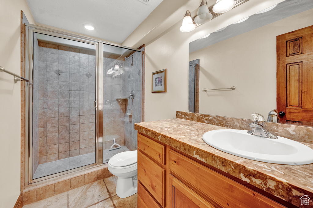 Bathroom featuring toilet, large vanity, tile floors, and an enclosed shower
