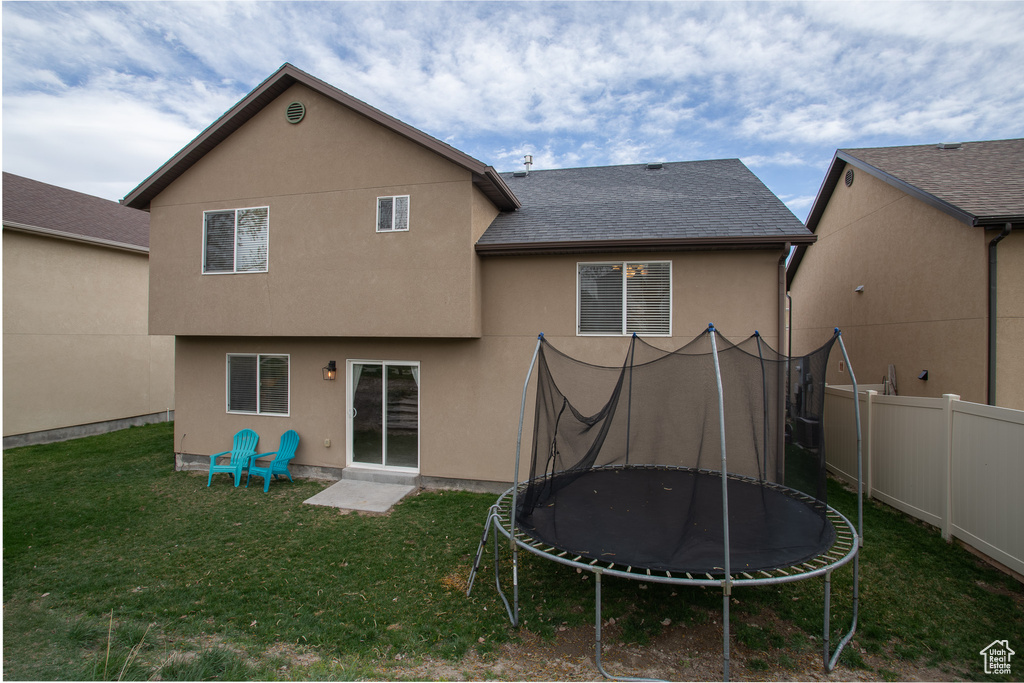 Back of property with a lawn and a trampoline