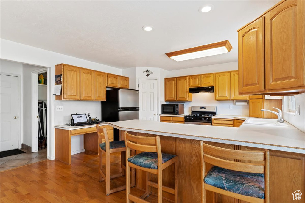 Kitchen with stainless steel appliances, a kitchen bar, fume extractor, light hardwood / wood-style flooring, and sink