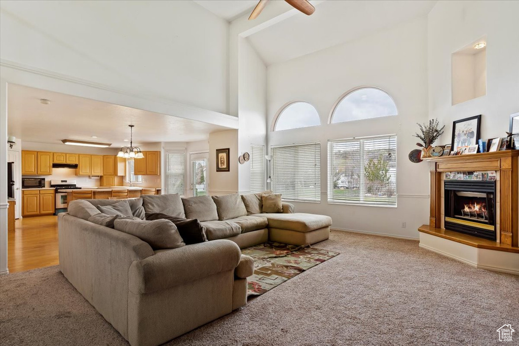 Living room with light colored carpet, high vaulted ceiling, and ceiling fan with notable chandelier