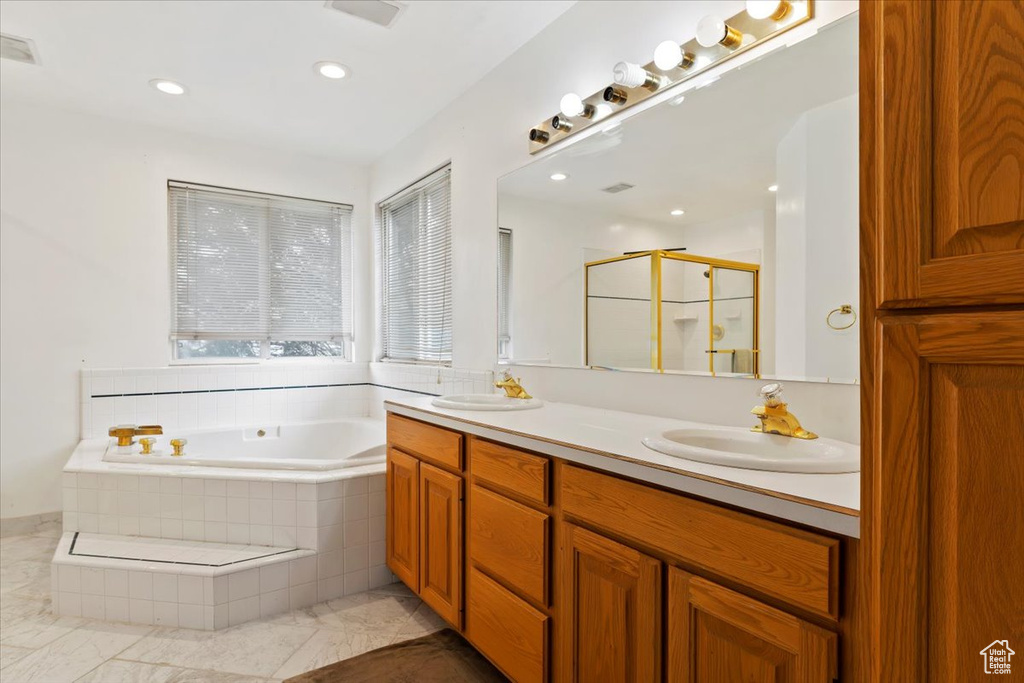 Bathroom with tile floors, dual sinks, vanity with extensive cabinet space, and separate shower and tub