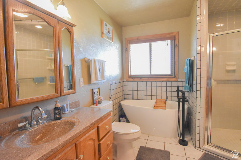 Bathroom featuring tile walls, a shower with door, tile flooring, vanity with extensive cabinet space, and toilet