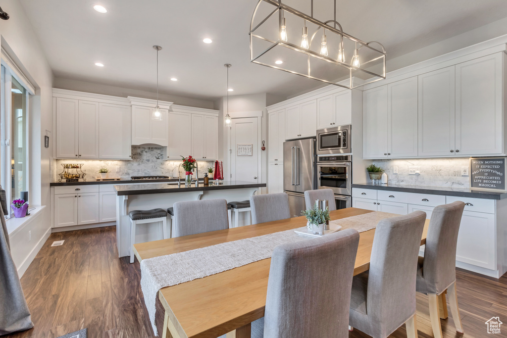 Kitchen with white cabinets, dark wood-type flooring, stainless steel appliances, and tasteful backsplash