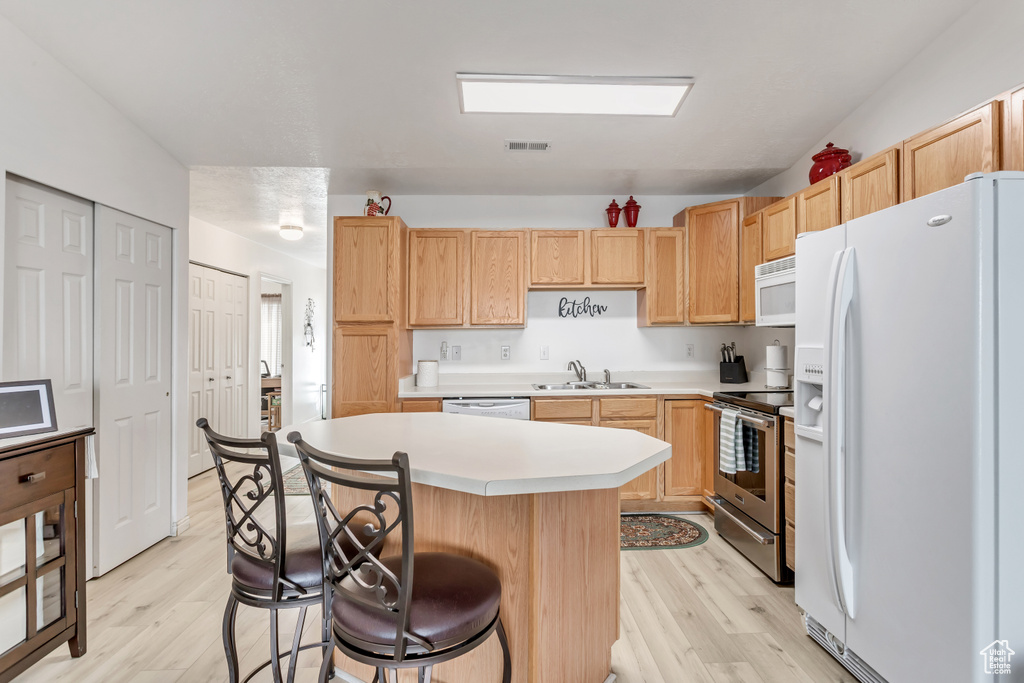 Kitchen featuring a center island, a breakfast bar area, white appliances, and light wood-type flooring