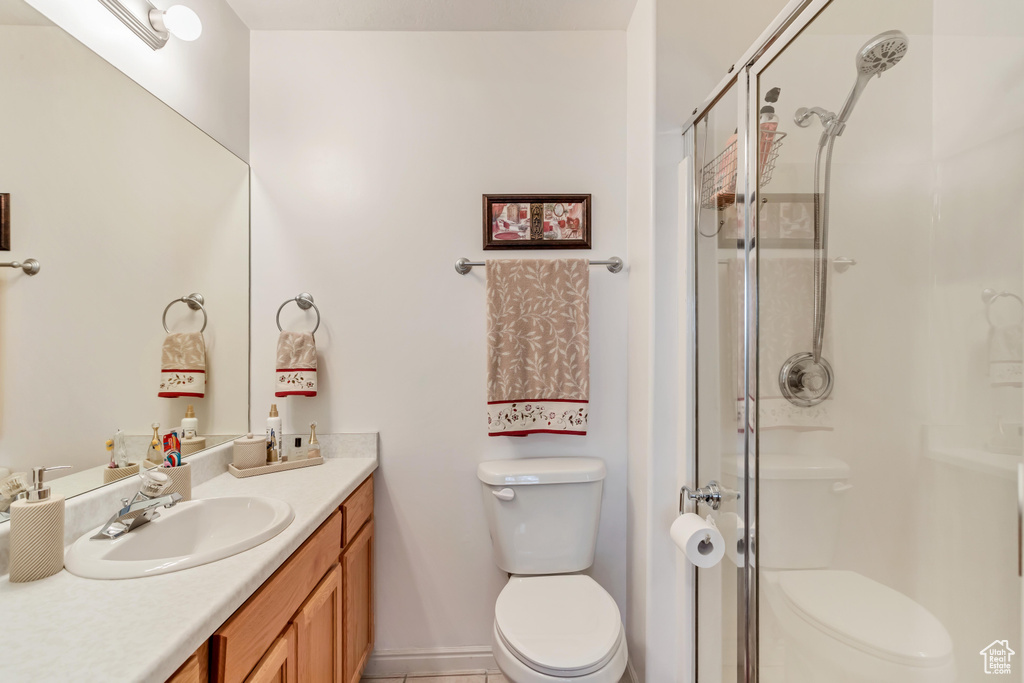 Bathroom with an enclosed shower, toilet, vanity, and tile flooring