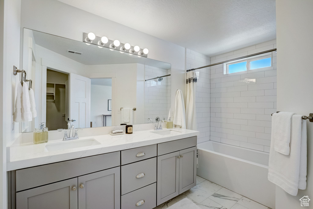 Bathroom with a textured ceiling, tile floors, dual vanity, and tiled shower / bath
