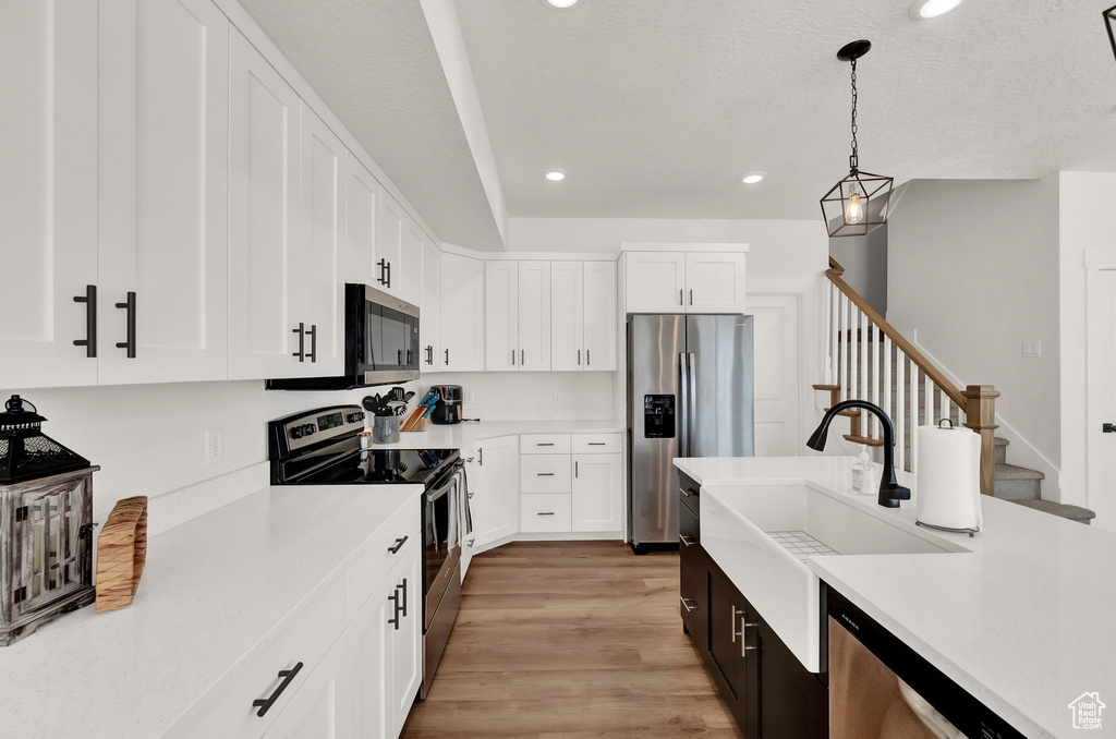 Kitchen with white cabinetry, light hardwood / wood-style flooring, stainless steel appliances, and pendant lighting