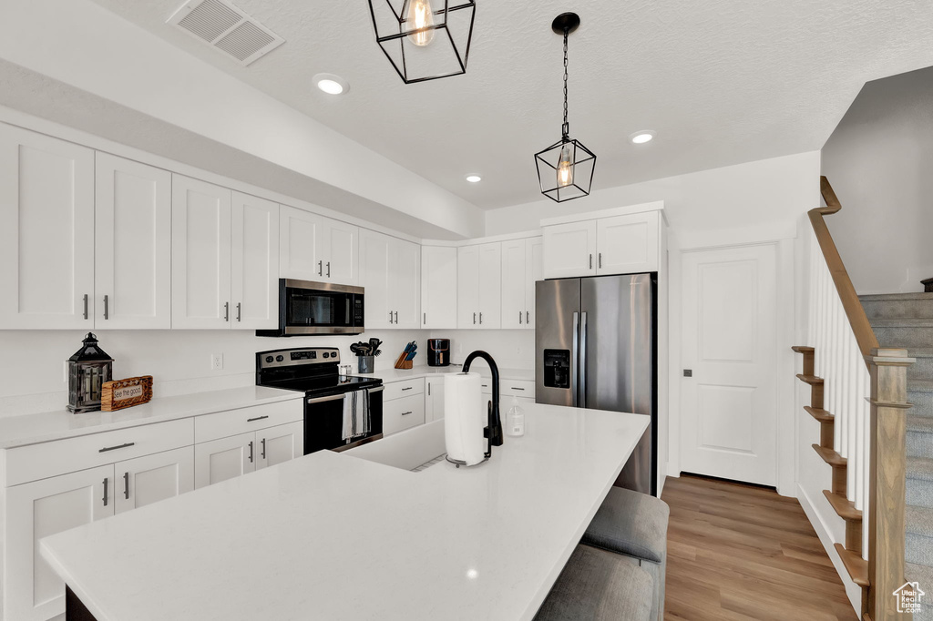 Kitchen featuring pendant lighting, stainless steel appliances, light hardwood / wood-style floors, a center island with sink, and white cabinets