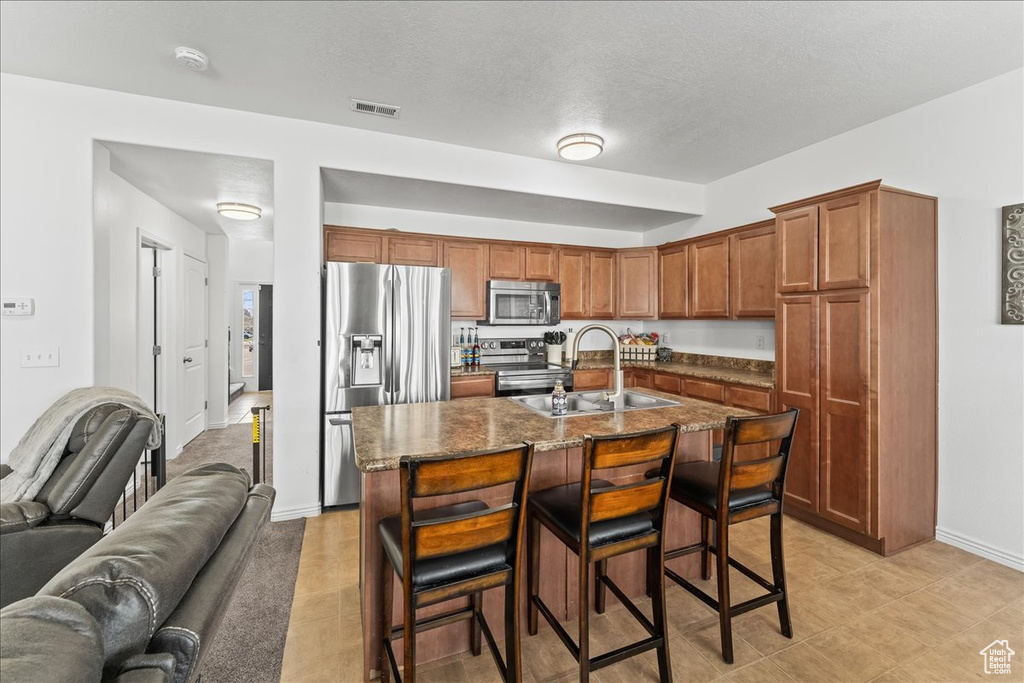 Kitchen with stainless steel appliances, light tile floors, a breakfast bar, a kitchen island with sink, and sink