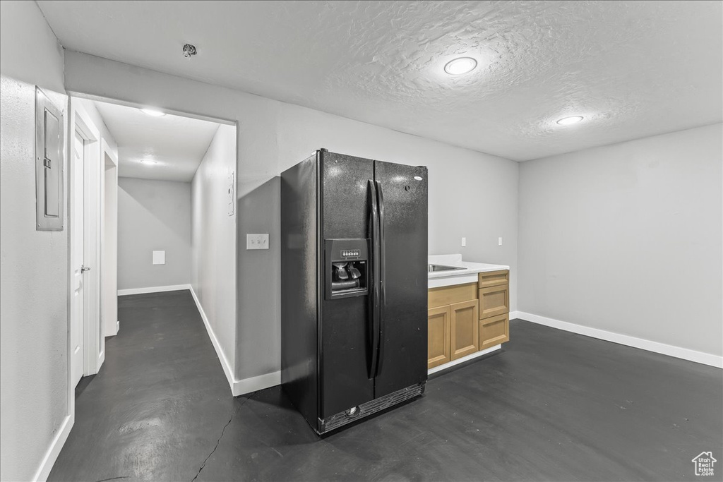 Interior space featuring light brown cabinets, black fridge, and a textured ceiling