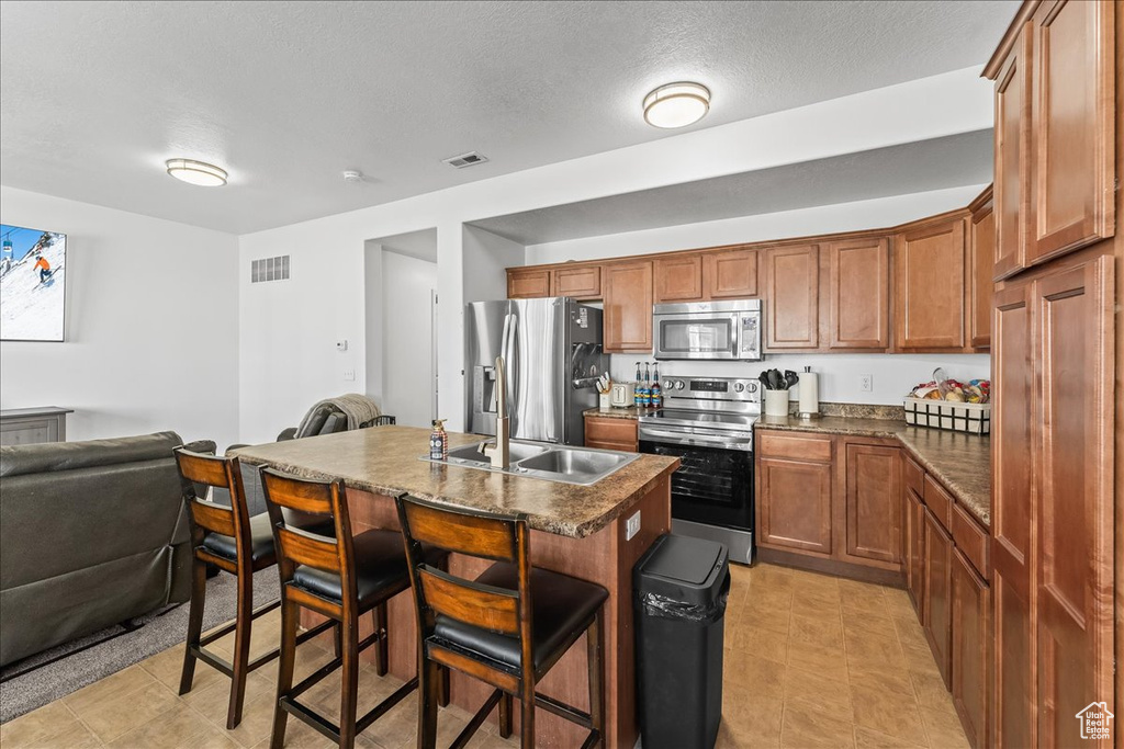 Kitchen featuring a breakfast bar area, stainless steel appliances, a center island with sink, and light tile floors