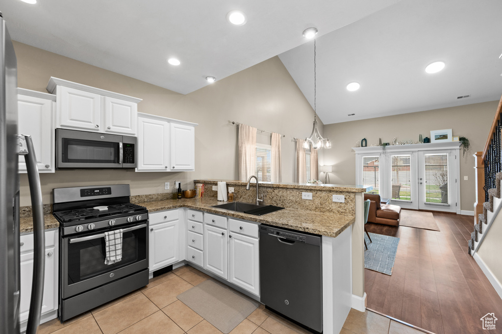 Kitchen featuring stainless steel appliances, light stone countertops, kitchen peninsula, white cabinetry, and sink