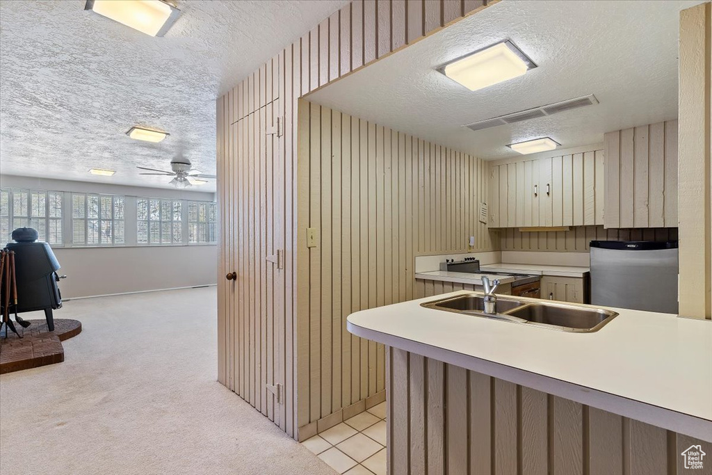 Kitchen with ceiling fan, sink, light carpet, refrigerator, and a textured ceiling