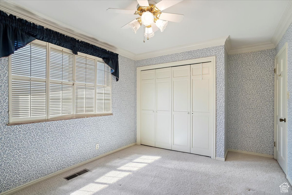 Unfurnished bedroom featuring a closet, ornamental molding, light colored carpet, and ceiling fan