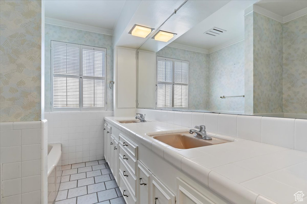 Bathroom with vanity with extensive cabinet space, tile walls, dual sinks, tile floors, and a tub