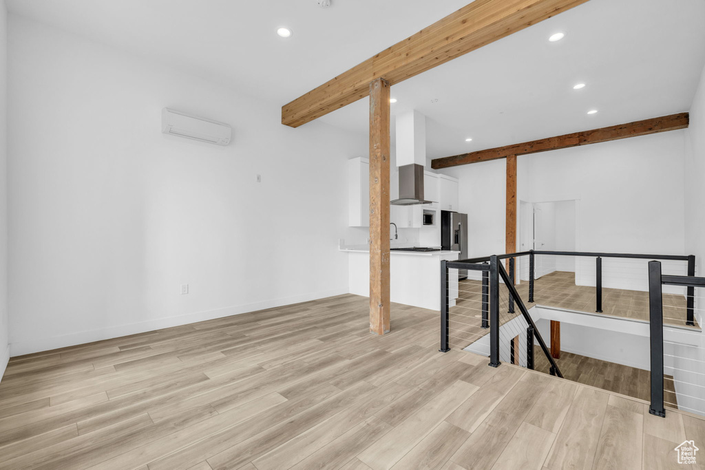 Interior space with a wall unit AC, light hardwood / wood-style flooring, and beam ceiling