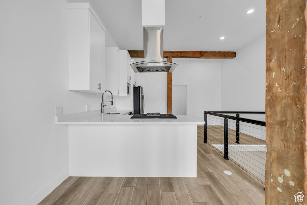 Kitchen with kitchen peninsula, white cabinetry, stainless steel appliances, and light hardwood / wood-style flooring