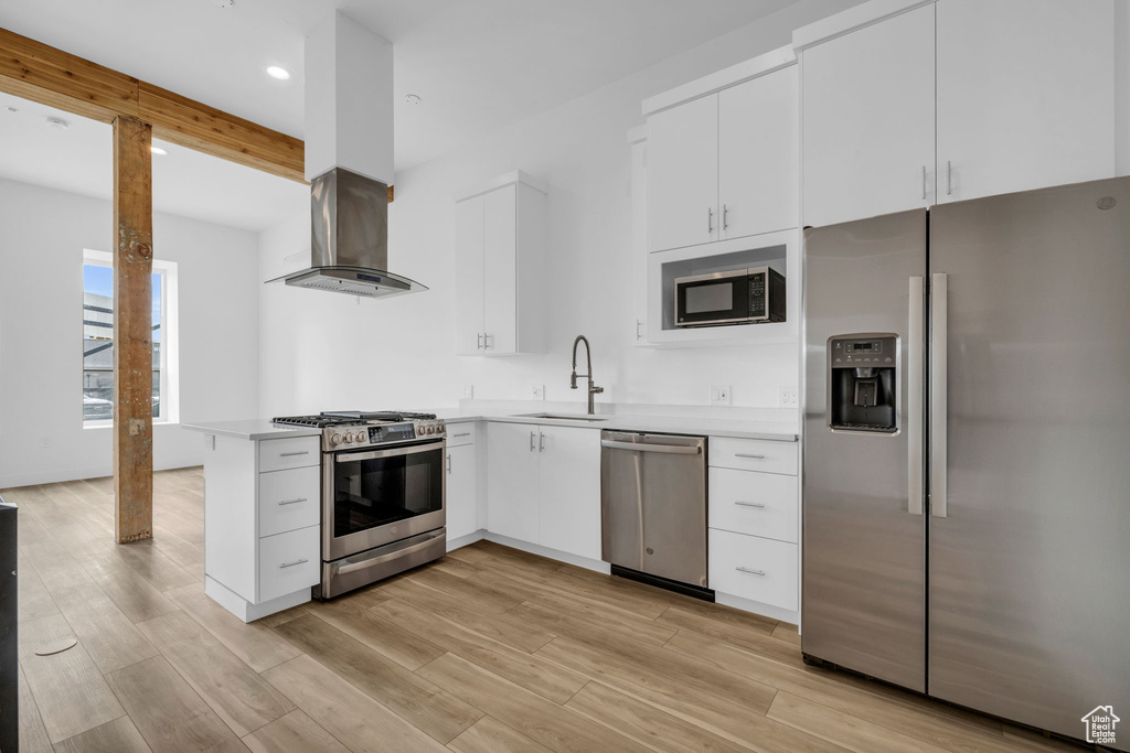 Kitchen with appliances with stainless steel finishes, sink, island exhaust hood, white cabinetry, and light hardwood / wood-style flooring