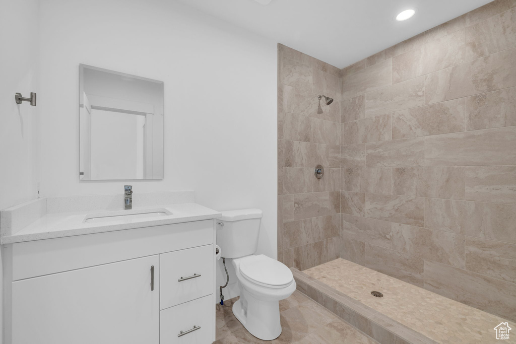 Bathroom with tile flooring, tiled shower, toilet, and vanity