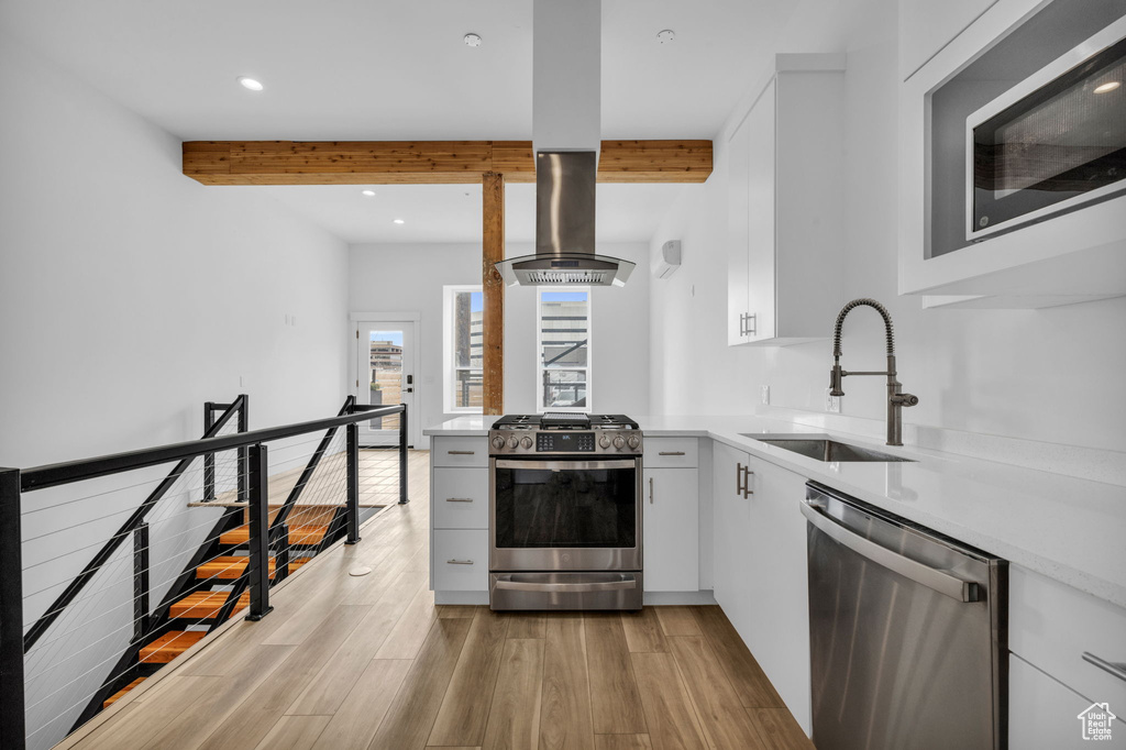 Kitchen featuring light wood-type flooring, stainless steel appliances, beam ceiling, sink, and white cabinets
