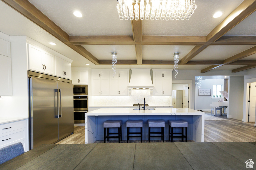 Kitchen with a chandelier, light hardwood / wood-style floors, white cabinets, built in appliances, and custom range hood