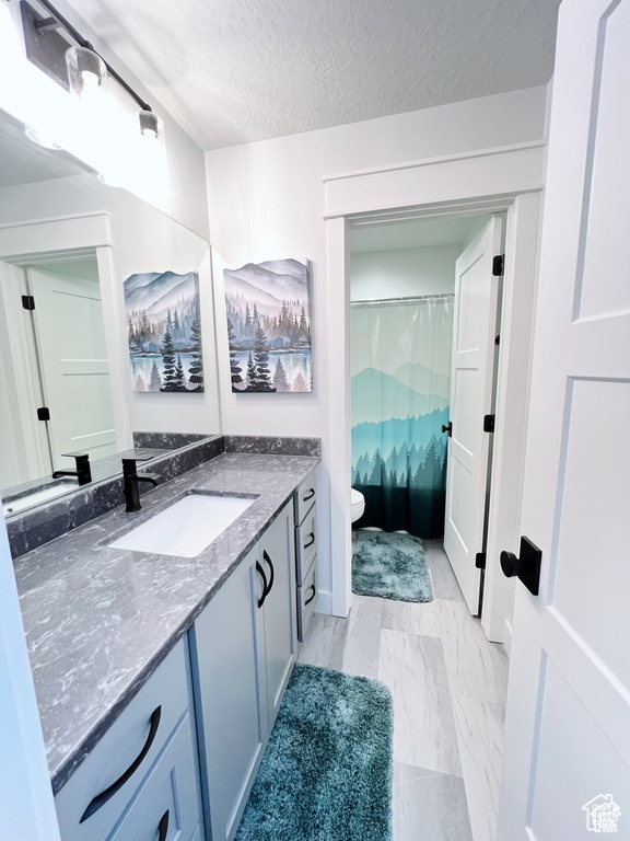 Bathroom featuring a textured ceiling, toilet, tile floors, and vanity with extensive cabinet space