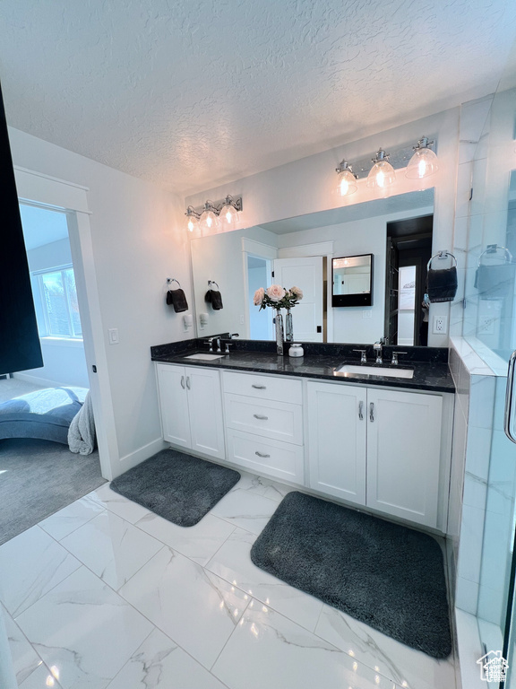 Bathroom with a textured ceiling, oversized vanity, tile floors, and dual sinks