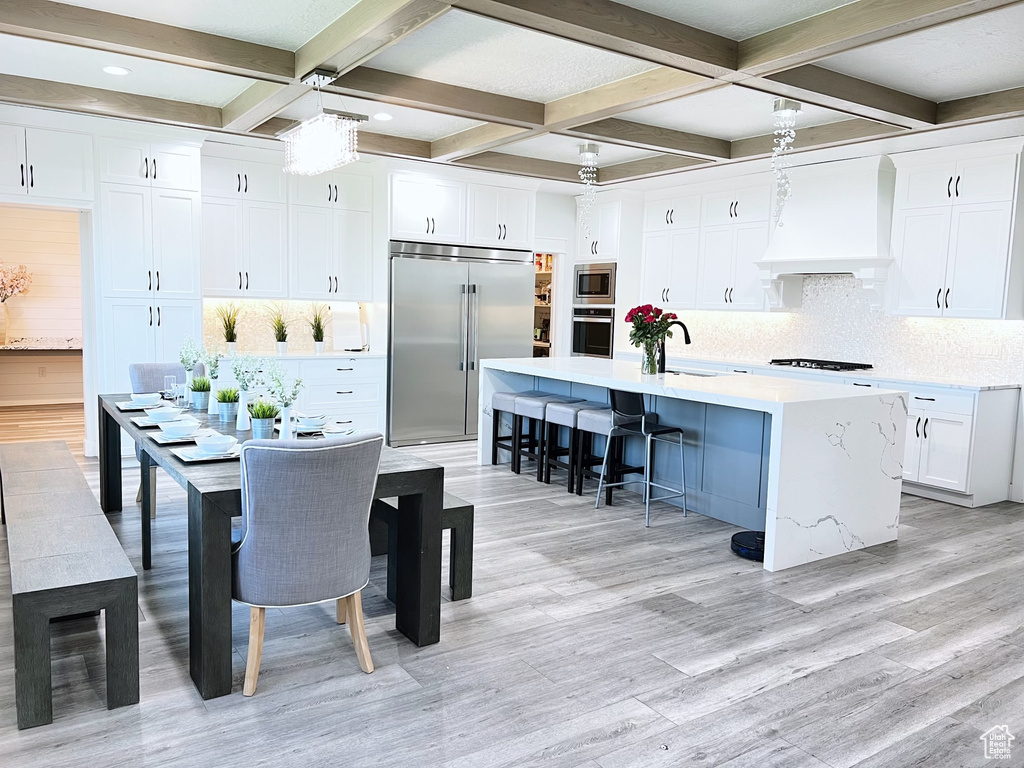 Kitchen featuring built in appliances, custom exhaust hood, an island with sink, and white cabinetry