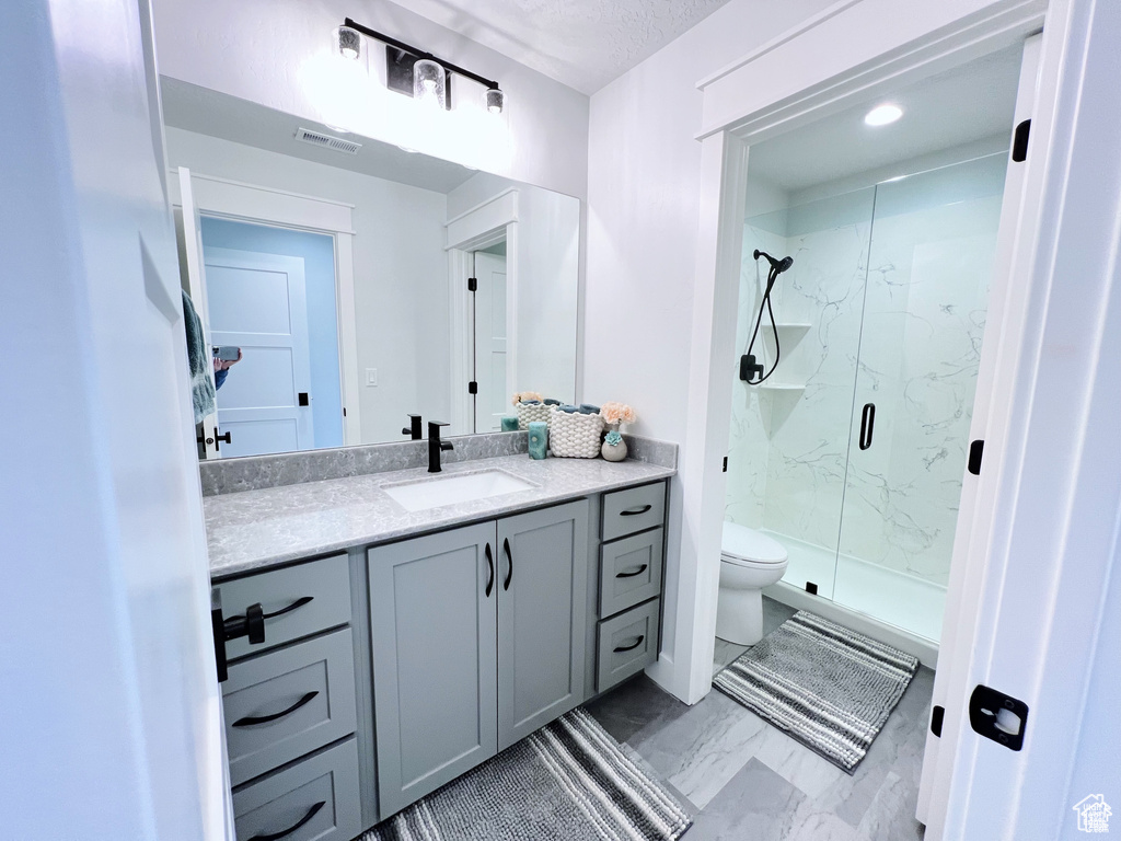 Bathroom with an enclosed shower, vanity, tile floors, and toilet