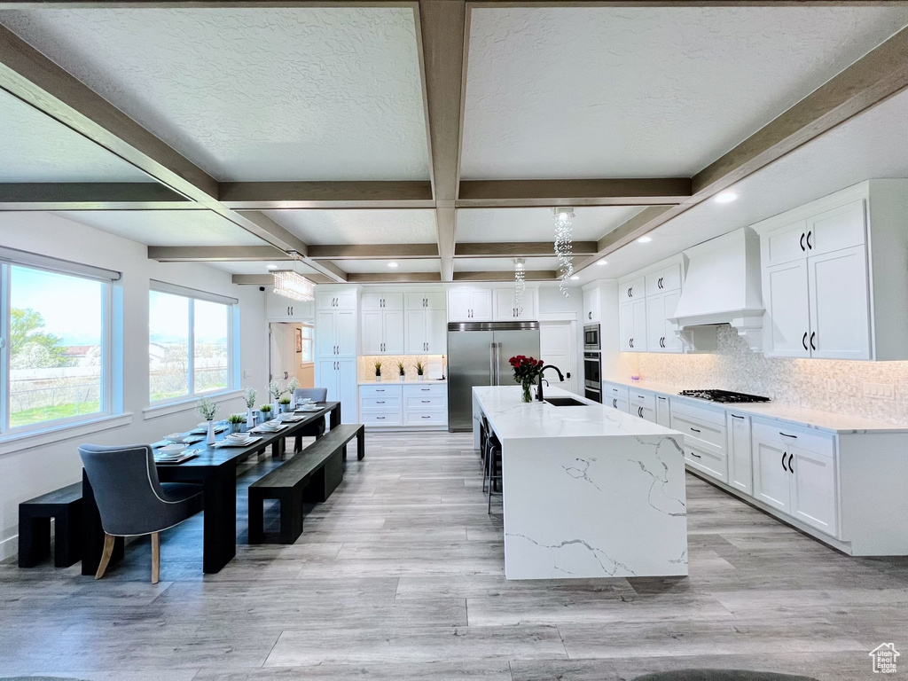 Kitchen with coffered ceiling, appliances with stainless steel finishes, premium range hood, and white cabinetry