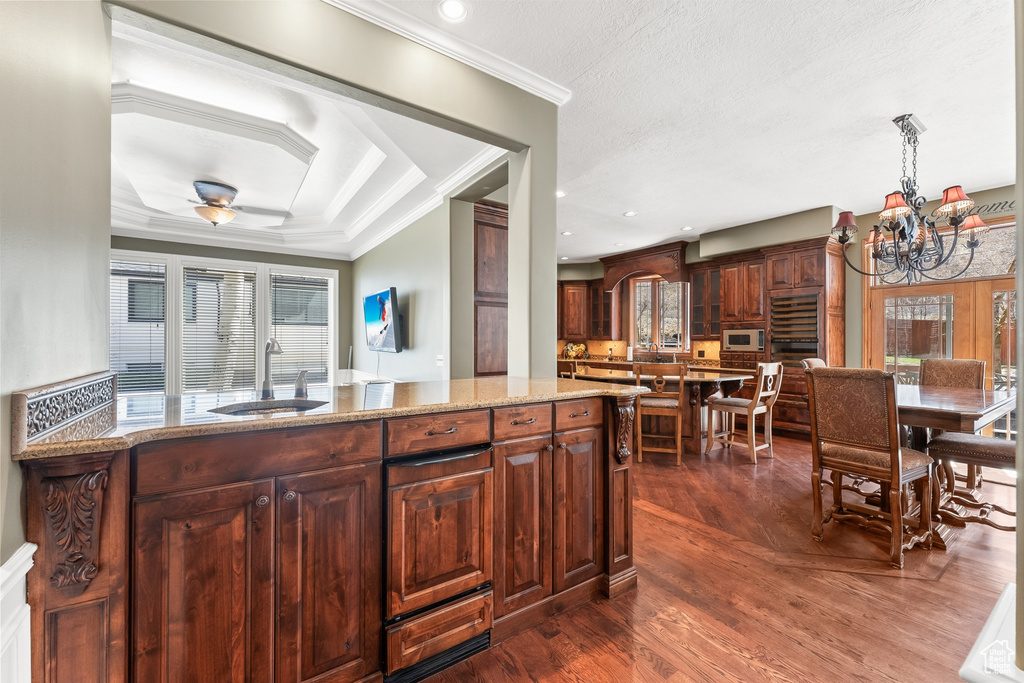 Kitchen featuring decorative light fixtures, dark hardwood / wood-style floors, ceiling fan with notable chandelier, light stone counters, and ornamental molding