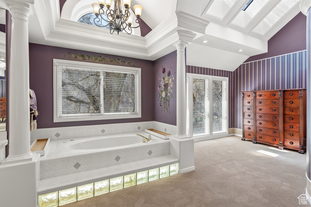 Bathroom with tiled bath, decorative columns, a notable chandelier, and ornamental molding