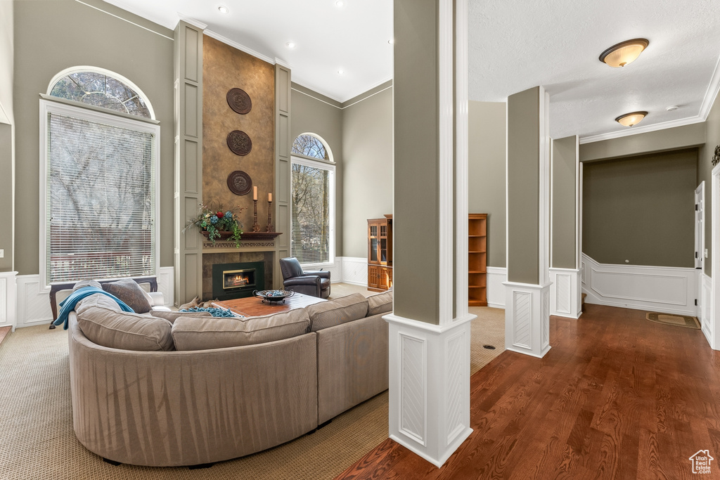 Living room with a fireplace, crown molding, dark wood-type flooring, and decorative columns